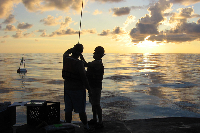 two people on the deck of a ship with a buoy in the background