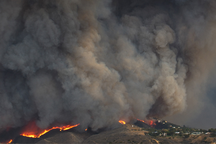 a cloud of smoke billows over a line of fire in hilly terrain