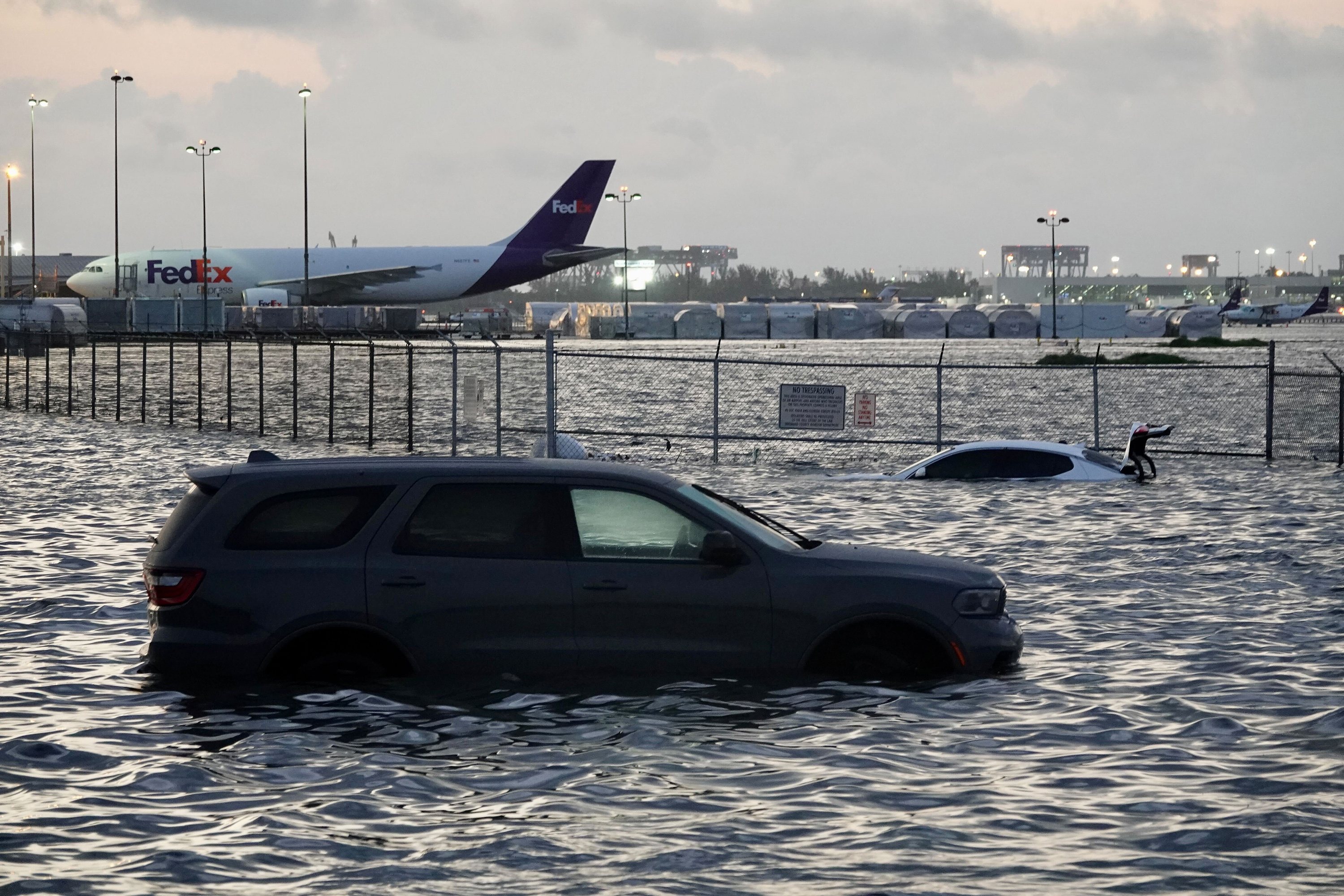 Photograph of a car flooded at an airport with a second vehicle and planes in the background in Florida.