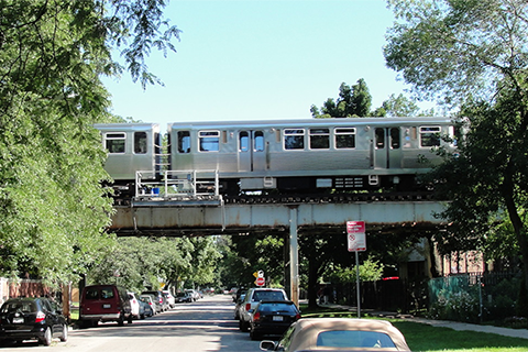 A tree-lined street crossed by an elevated train track