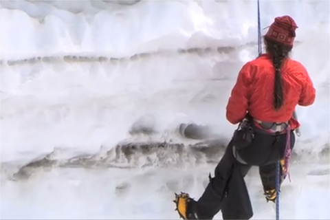 Photo of a researcher hanging by a rope into a snowpit that shows layers of soot